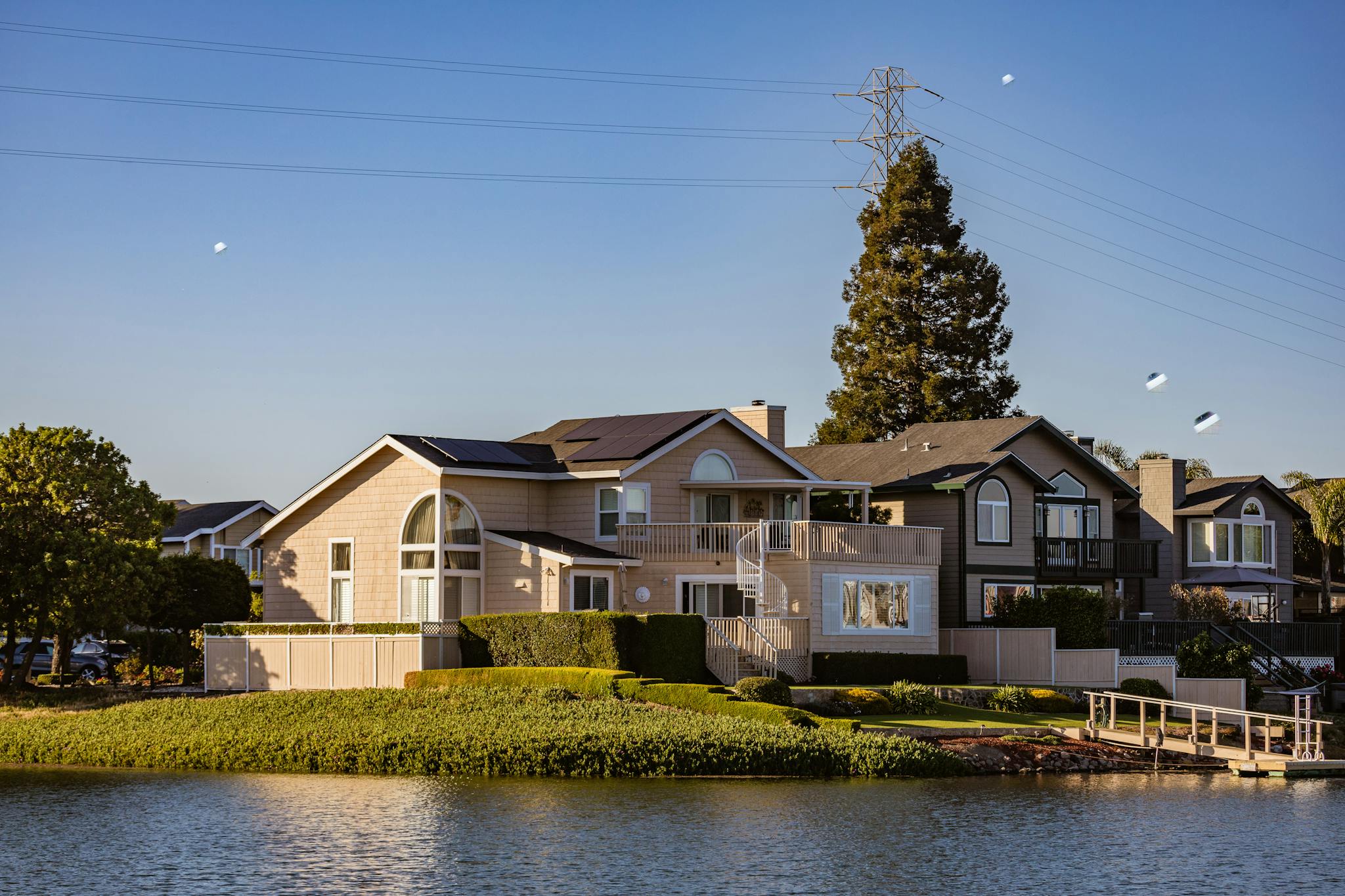 Stunning modern houses line a serene riverbank with clear blue skies, showcasing beautiful architecture and nature.